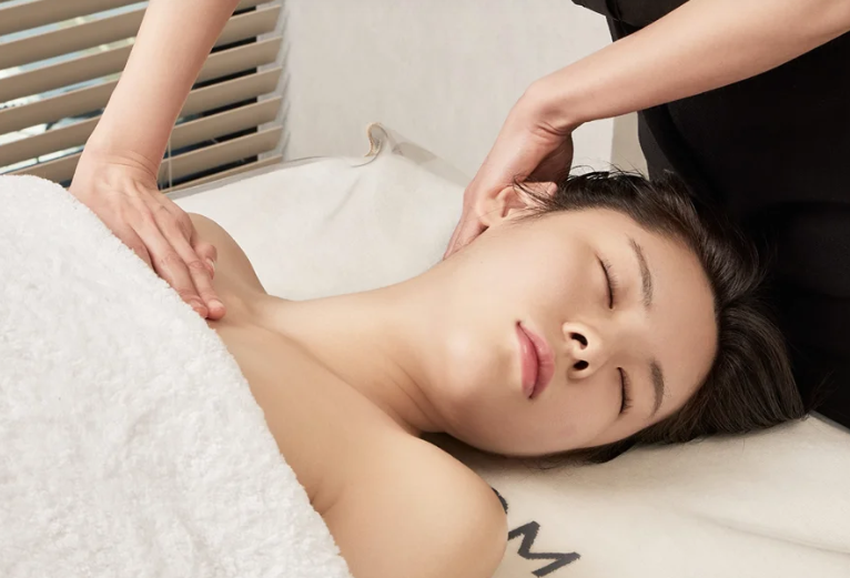 여성이 침대에 누워 승모근 경락 마사지를 편안하게 받고 있다.
